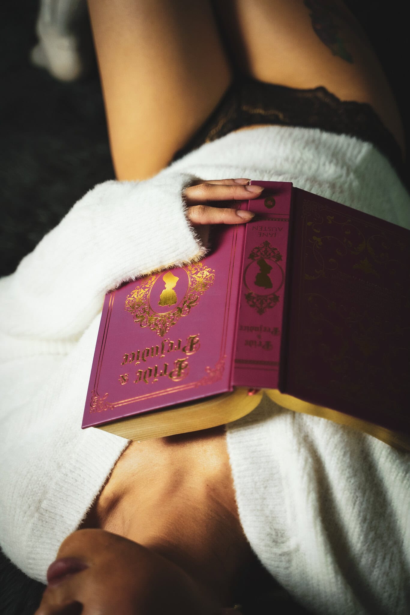 A person sitting comfortably while holding an ornate, burgundy book with gold embossing, resting on their lap covered with a white towel. Image by Rya Eisma of Shamelessly Sexy Boudoir Photography, Las Vegas, NV