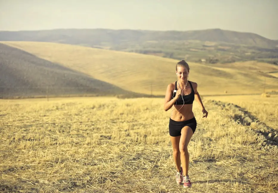 A woman is jogging through a dry, grassy field with hills in the background. She is wearing black athletic wear and earphones, under a clear sky. The scene is bright and sunny, conveying a sense of energy and freedom. Image by Rya Eisma of Shamelessly Sexy Boudoir Photography, Las Vegas, NV