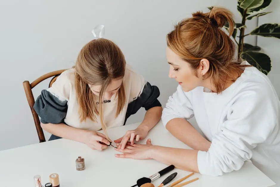 A young girl is painting the nails of a woman sitting beside her at a white table. The table has various nail polish bottles and brushes. Both appear focused on the task. There's a plant in the background. Image by Rya Eisma of Shamelessly Sexy Boudoir Photography, Las Vegas, NV